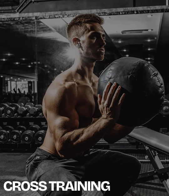 Hombre entrenando con un balón medicinal en un gimnasio, con mancuernas al fondo y el texto “CROSS TRAINING” en la parte inferior.