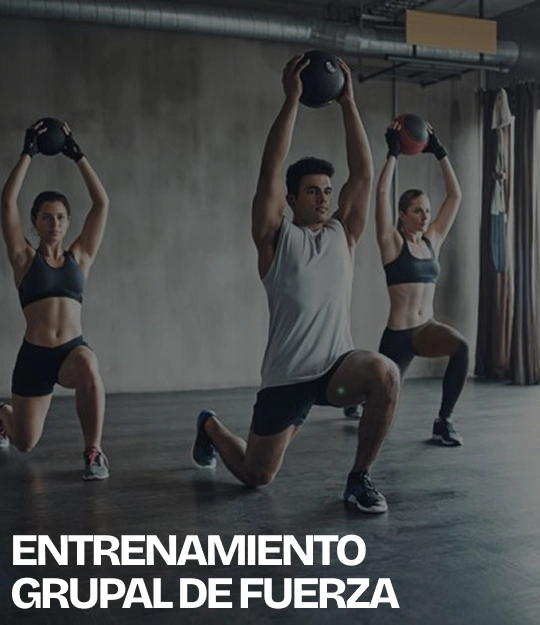 Tres personas realizan zancadas con balones medicinales elevados sobre la cabeza en un gimnasio, con el texto “ENTRENAMIENTO GRUPAL DE FUERZA” en la parte inferior.